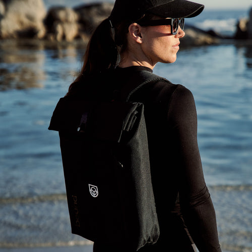 Roll-Top Backpack in orange held out in one hand, low angle