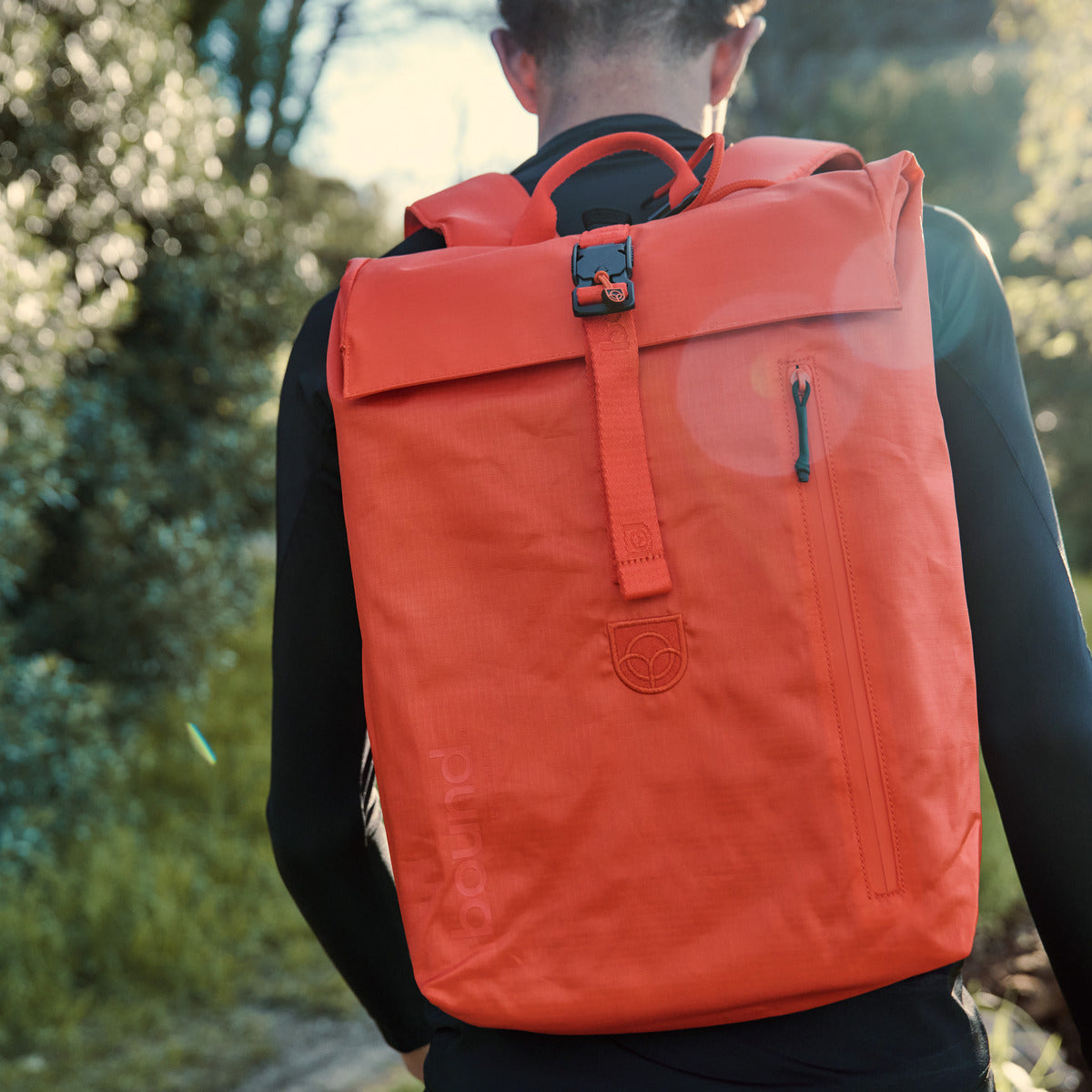 Roll-Top Backpack in orange worn on the back by a man walking along a cliff