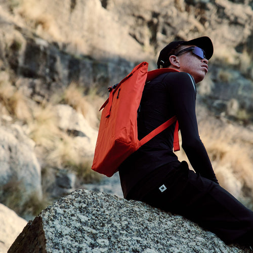 Roll-Top Backpack in orange worn on the back by a man in grassland, rear view