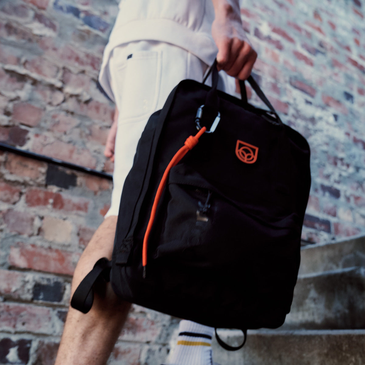 Town Backpack in black worn on the back by a woman walking past a stone building