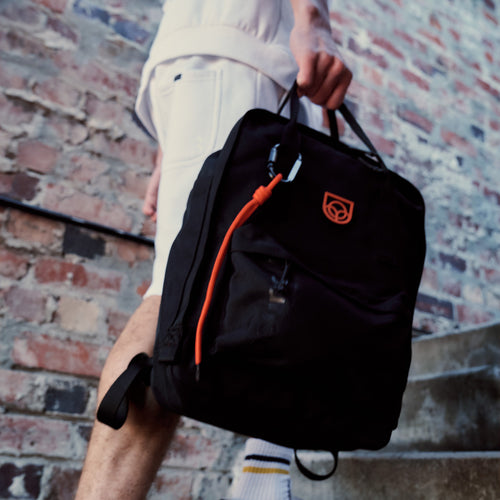 Town Backpack in black worn on the back by a woman walking past a stone building