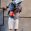 Town Sling Bag in black worn crossbody by a man in a white t-shirt on a city street