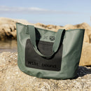 NSRI Tote in green standing on coastal rocks with the sea behind