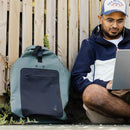 NSRI Backpack in green standing beside a man working on a laptop against a wooden fence