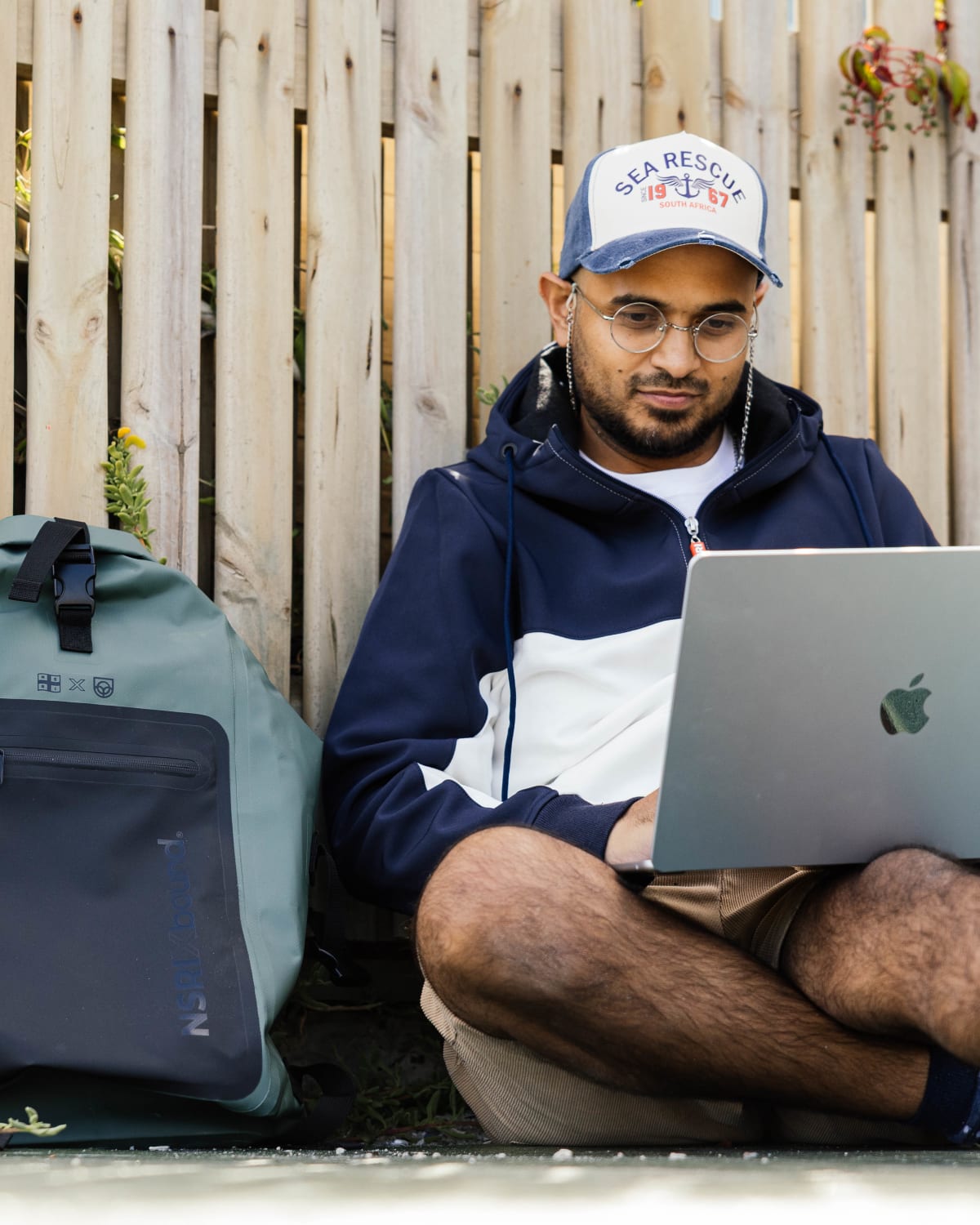 NSRI x Bound waterproof backpack beside a laptop, portrait crop