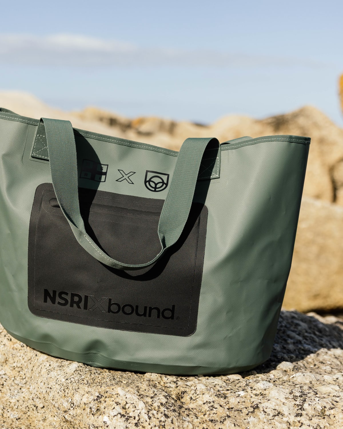 NSRI x Bound waterproof tote on coastal rocks, portrait crop